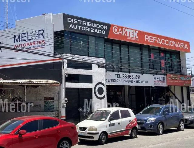 Esquina de Melor Autopartes con el logotipo pintado en el muro lateral y el auto de reparto rotulado estacionado enfrente