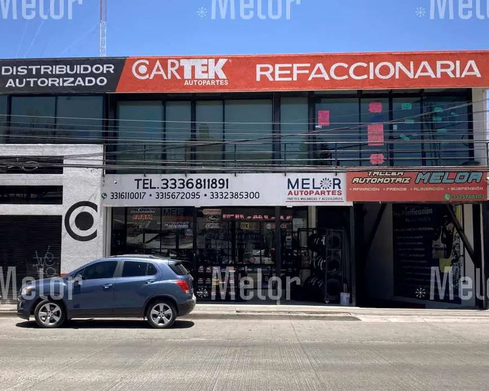 Fachada de Melor Autopartes sobre Av. Río Nilo: rótulo rojo de distribuidor autorizado Cartek y refaccionaria arriba, y abajo los teléfonos de la tienda y la entrada del taller